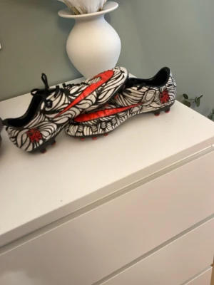 Nike Mercurial fotbollsskor svart/vit/röd - Säljer ett par Nike Mercurial fotbollsskor med grymt mönster i svart och vitt samt röda detaljer och sula. Skorna har låg profil, snörning och är tillverkade i syntetmaterial för bästa grepp och känsla på planen. Perfekta för dig som vill sticka ut på fotbollsplanen.