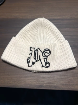 Vit ribbstickad mössa Palm Angels - Snygg vit ribbstickad mössa från Palm Angels med svart broderad logga framtill. Tillverkad i en mjuk ull- och akrylblandning som håller dig varm. Perfekt accessoar för att lyfta din streetwear-stil.