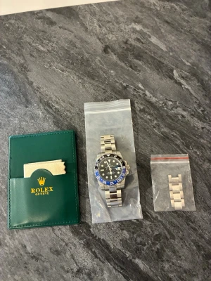 Herr klocka  - Säljer en herr klocka GMT ' med svart och blå vridring, svart urtavla och Oyster-länk i rostfritt stål. Klockan har klassisk sportig design och kommer med extra länkbitar samt originalfodral och putsduk.