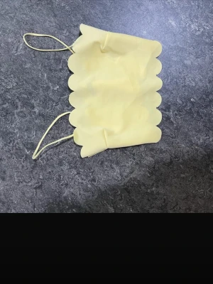 Gul scallop-kantad stringtrosa - Säljer en ljusgul stringtrosa med dekorativa scallop-kanter och tunna sidoband. Materialet är mjukt och stretchigt, perfekt för dig som vill ha något diskret och bekvämt. Ingen synlig logga eller märke.