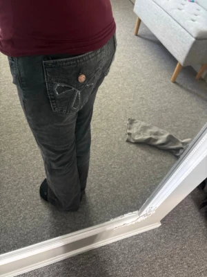 Gråa bootcut jeans med dekorerad ficka - Säljer ett par gråa bootcut jeans med snygg dekorsöm och knappdetalj på bakfickan. Jeansen har klassisk femficksmodell och är tillverkade i mjukt denimtyg. Perfekta för dig som gillar en avslappnad men trendig look.