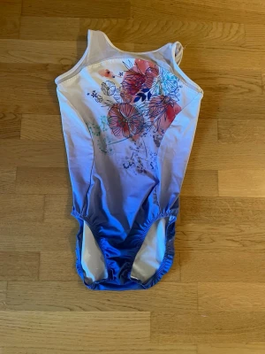 Blåvit gymnastikdräkt med blommönster - Snygg gymnastikdräckt i blått och vitt med blommigt mönster framtill och bak. Axelbanden är smala och modellen är klassisk med rundad hals. Materialet är stretchigt och passar perfekt för gymnastik eller tävlingar.