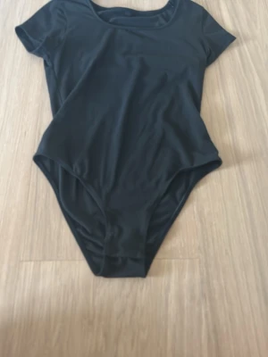 Svart kortärmad body - En stilren svart body med korta ärmar och rund halsringning. Tillverkad i ett stretchigt och mjukt material som sitter bekvämt mot kroppen. Perfekt för att skapa en clean och enkel look.