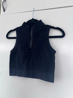 Svart croppad ärmlös med dragkedja, storlek S - Svart croppad topp med halv dragkedja framtill. Tight passform, perfekt till jeans eller som sporttopp. Materialet är stretchigt. Köpt i Australien - storlek 8/S. 📏 Midjevidd: 31cm