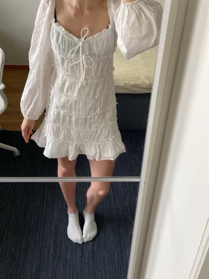 Vit sommarklänning från Gina - En oanvänd klänning med rosett band framifrån och vida armar. Tyget är mönstrade med blommor och har en figurnära form. Den är hyfsat kort i längden och har en kjol under så den är inte genomskinlig. Skicka gärna prisförslag! 