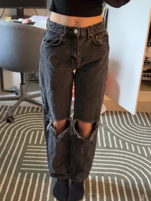 Svarta ripped jeans från Gina Tricot - Säljer ett par svarta jeans från Gina Tricot i modellen perfect jeans. De har hög midja, raka ben och stora slitningar över knäna för en trendig look.