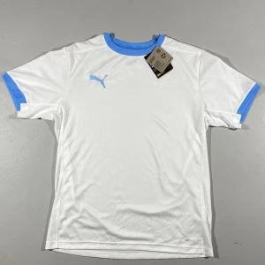 Vit sport T-shirt Puma  - Snygg vit sporttröja från Puma med ljusblå logga, krage och ärmslut. Tillverkad i återvunnet material med DryCell-teknologi som håller dig torr under träningen. Perfekt för fotboll eller gym.