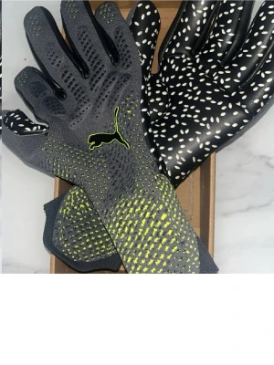 Puma grå/gula sporthandskar - Säljer ett par sportiga handskar från Puma i grått med gula detaljer och svart logga. Insidan är svart med vita prickar för extra grepp. Tillverkade i syntetmaterial och har en modern, tight passform.