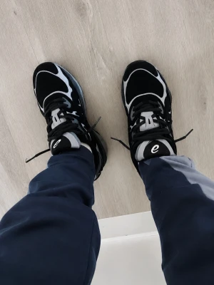 Svarta sneakers från Etnies - Snygga svarta sneakers från Etnies med vita och grå detaljer. Skorna har en klassisk låg siluett, tjock vit sula och svart ovandel i mocka och textil. Etnies-logga på plösen och sköna snörningar för perfekt passform.