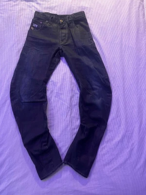 Mörkblå G-Star RAW jeans - Säljer ett par mörkblå jeans från G-Star RAW med klassisk femficksdesign och snygga sömdetaljer på benen. Jeansen har en rak passform och är tillverkade i slitstarkt denimtyg. Perfekta för dig som gillar streetwear och en modern look.