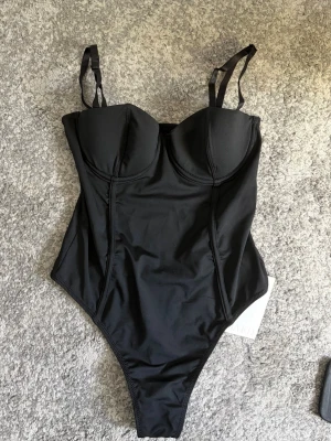 Svart baddräkt med bygel och axelband - Snygg svart body från nakd, passar till en fin middag/ fest till ett par snygga jeans. Säljs pågrund av att jag köpte fel storlek , men den är jätte snygg och passar till det mesta! Original pris 400