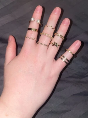 Guldiga ringar med pärldetaljer - Säljer ett set med flera tunna och breda ringar i guldton, vissa med vågig design, en med små pärlor och en med bladformad detalj. Perfekt för dig som gillar att mixa och matcha olika stilar på fingrarna.