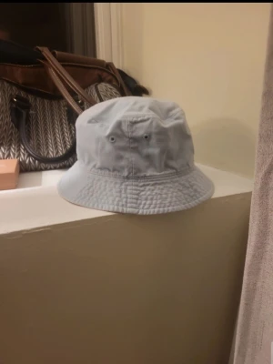 Ljusblå bucket hat i bomull - Snygg ljusblå bucket hat i mjuk bomull med klassisk form och bred brätte. Hatten har två ventilationshål på sidorna och är perfekt för en avslappnad streetstyle-look. Insidan är ljusrosa vilket ger en cool kontrast.