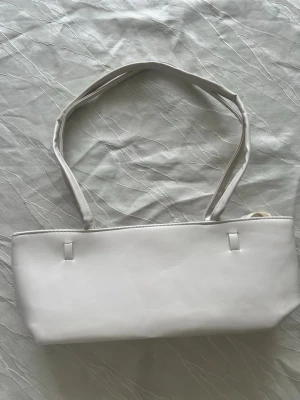 Vit axelväska i minimalistisk stil - Snygg vit axelväska med enkel och stilren design. Väskan har rektangulär form och dubbla axelband. Tillverkad i slätt material som ger en clean look. Perfekt för dig som gillar minimalistiska accessoarer och vill ha en väska som passar till många outfits. Pris kan diskuteras 
