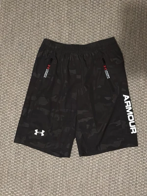 Under Armour shorts - Otroligt snygga svarta shorts från Under Armour. Resår i midjan, snören innanför shortsen och dragkedjefickor med röda detaljer.