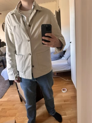 Beige overshirt med stora fickor - Snygg beige overshirt med klassisk krage och tre stora utanpåfickor framtill. Jackan har raka ärmar och stängs med knappar. Perfekt att slänga över en t-shirt eller hoodie för en clean look. Materialet känns slitstarkt och passar till jeans eller chinos.