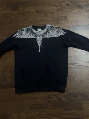  Marcelo Burlon äkta - Svart sweatshirt från Marcelo Burlon med ikoniskt vitt vingtryck över axlar och halsringning. Tröjan har rund hals och långa ärmar. Perfekt för dig som gillar streetwear och vill sticka ut med en unik design.