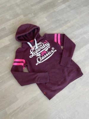 Superdry hoodie vinröd dam - Den är riktigt snygg och trendig. Den är i använt skick och trycket är skrynkligt. Kolla på bilderna. 