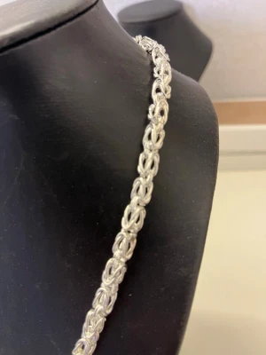Silverfärgat kedjehalsband - Snyggt halsband i silverfärg med en robust, flätad kedjedesign. Halsbandet har en klassisk och tidlös look som passar perfekt till olika stilar. Materialet ser ut att vara metall och länkarna är tätt sammanflätade för en cool effekt.