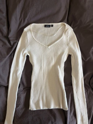 Ribbad vit långärmad topp KappAhl - Ribbad vit långärmad topp från KappAhl med v-ringad hals. Toppen är figurnära och har en mjuk, stretchig känsla. Perfekt att styla med alla underdelar.