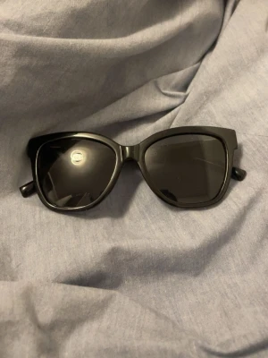 Svarta solglasögon med bred båge - Stilrena svarta solglasögon med bred båge och klassisk form. Perfekta för att ge en cool touch till din outfit. Glasögonen har helsvarta bågar och mörka linser. Passar dig som gillar en enkel men trendig look.