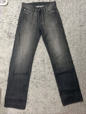 Grå raka jeans med tvättad look - Snygga grå jeans med rak passform och tvättad effekt. Klassisk femficksmodell med bälteshällor och knappgylf. Jeansen har en cool, något sliten look som passar perfekt till en avslappnad stil. Materialet är denim i bomull.