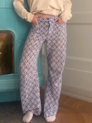 Mönstrade blåvita loungewear-byxor - Säljer ett par mjuka och sköna loungewear-byxor med blått och vitt grafiskt mönster. Byxorna har rak passform, resår i midjan med knytband och är perfekta för chill hemma. Materialet känns lätt och bekvämt mot huden.