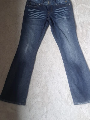 Blå bootcut jeans med slitningar - Så fina blåa jeans med fina detaljer vid fickorna och knapparna! Lågmidjade bootcut. Måtten: Gren: 19 cm Midja:37 innerben:80 Tveka inte att fråga om något! Pris går att diskuteta🩵💙🩵