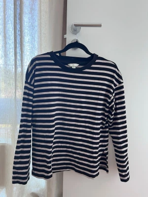 Randig långärmad topp från H&M - Snygg långärmad topp från H&M i svart och vitt med klassiskt horisontellt randigt mönster. Tillverkad i mjuk bomull och har en rund halsringning. Perfekt att styla med jeans eller kjol för en cool vardagslook.