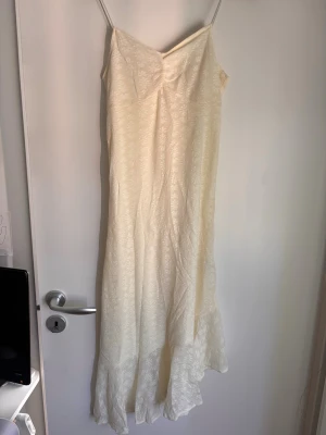 Asymmetrisk klänning i spets Nelly - Asymmetrisk klänning i spets. Klänningen har ett vackert blommigt spetsmönster och faller mjukt ner mot golvet. Perfekt för sommaren. Aldrig använd från Nelly. Den är cremefärgad/benvit