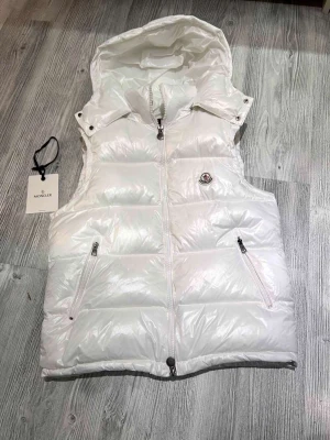 Moncler väst vit - Hej! Jag säljer nu min vita moncler väst som är i nyskick den är andvänt väldigt sparsamt och inte alls länge, den är  äkta och köpt ifrån Nk kvittot finns som bevis till det och nfc Scan funkar som den ska. original tillbehören ingår med jackan som taggarna og plastpåsen och dustbagen, priset är hugget i Sten hör av dig vid minsta lilla fråga!😄