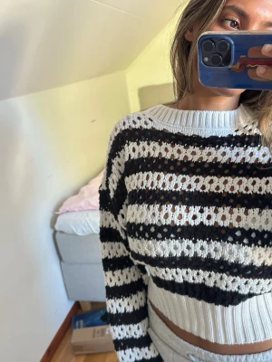 Svartvit stickad cropped tröja - Säljer en stickad cropped tröja med svartvita ränder och hålmönster. Tröjan har rund halsringning, långa ärmar och ribbade muddar. M men passar S!!!💕