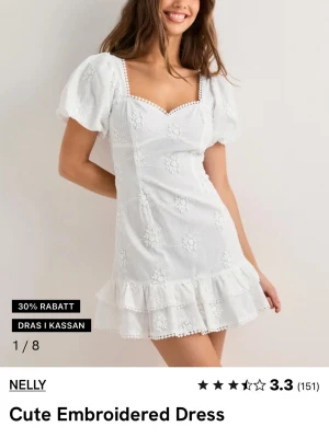 Vit klänning från Nelly - Superfin vit kortklänning från Nelly med broderade blommor, puffärmar och volangkant nertill. Klänningen har v-ringning, öppen rygg med stor rosett och söta spetsdetaljer längs kanterna. Perfekt för skolavslutningen eller student!                      Helt ny med prislapp på!!! 