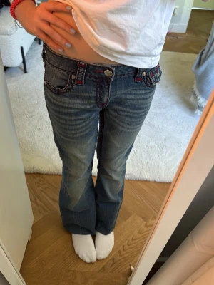 True Religion bootcut jeans blå - Snygga blå bootcut jeans från True Religion med röda kontrastsömmar och detaljerade fickor både fram och bak. I den här bilden har jag vikt upp dem men dem är i storlek 24. (Typ midwaisted)😘😘