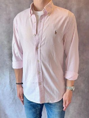 Randig Ralph Lauren Skjorta - Stl M, Slim Fit - Riktig snygg Ralph Lauren Skjorta i rosa och vitt, perfekt till sommaren! 🏖️🌊 | Mycket bra skick: 9,5/10, utan defekter  | Stl: M |  Modellen är 177cm och väger 74kg | Billigare pris vid köp av bundle 😉Hör av dig vid frågor // Galgen 🫡 