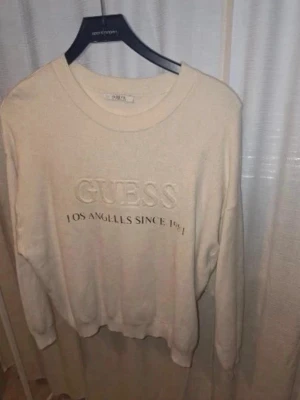 Beige sweatshirt från Guess - Beige sweatshirt från Guess med broderad logga och texten 'Los Angeles Since 1981' på bröstet. Tröjan har rund halsringning, långa ärmar och ribbade muddar vid ärmslut och nederkant. Perfekt för en avslappnad och stilren look.
