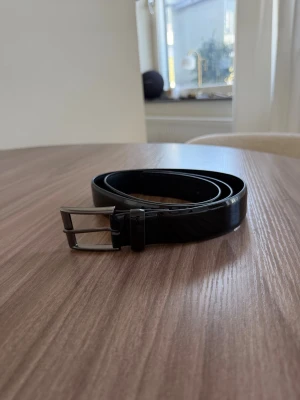 Bälte Pier One - Stilrent svart bälte från Pier One i äkta skinn med klassiskt silverfärgat spänne. Aldrig använt då det var för stort. GJORT ETT EGET HÅL!