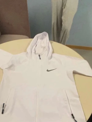 Vit hoodie från Nike  - Snygg vit hoodie från Nike framtill och klassisk svart Nike-logga på bröstet. Hoodien har huva med snörning och två fickor. Perfekt för en sportig och clean look.