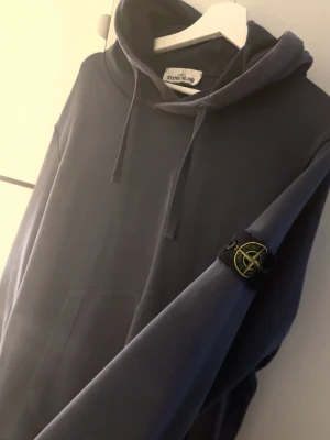 Mörkblå hoodie från Stone Island - Snygg mörkblå hoodie från Stone Island med klassisk huva och dragsko. Har den ikoniska loggan på vänster ärm och en stor magficka framtill. Skriv om du är intresserad kan visa att den är äkta också.