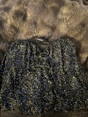 Glittrig svart paljett-topp Gina Tricot - Supersnygg svart topp från Gina Tricot täckt med glittrande paljetter. Bandeau-modell. Perfekt för dig som vill sticka ut och glänsa på nästa utekväll. Materialet är mjukt och stretchigt för skön passform.