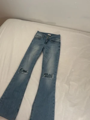 Ljusblå bootcut jeans från Nelly - Säljer ett par ljusblå bootcut jeans från Nelly med slitningar över knäna och klassisk femficksmodell. jeansen är hemma uppsydda och lagom till mig är 163, Jeansen har dubbla knappar i midjan och är tillverkade i mjukt denimtyg. Perfekta för en avslappnad och trendig look.
