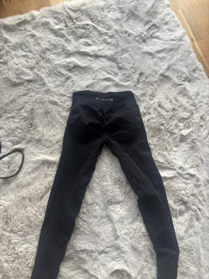 Svarta seamless leggings Relode - Säljer ett par svarta seamless leggings från Relode med hög midja och stretchigt material. Perfekta för träning eller chill. Diskret logga framtill i vitt. Sitter tight och formar sig efter kroppen. Storlek S tall
