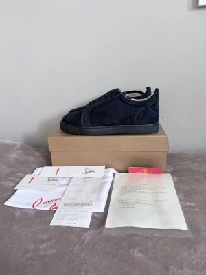 Christian louboutin - Snygga mörkblå sneakers från Christian Louboutin i mocka med klassisk röd sula. Skorna har en stilren design med lågt skaft och svarta snören. Perfekta för dig som vill sticka ut med exklusiva detaljer och lyxig känsla. Hör av er vid minsta fundering! Mvh Quadra Closet!