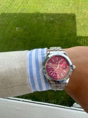 Klocka i rostfritt stål med rosa urtavla - Säljer en stilre klocka  med metallarmband i silver och en unik rosa urtavla med zebramönster. Klockan har datumvisning och klassisk rund boett. Perfekt accessoar för dig som vill sticka ut med färg och mönster.
