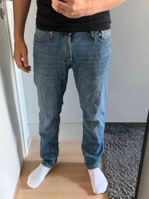 Blå raka jeans i klassisk modell - Säljer ett par blå jeans med rak passform och normal midja. Jeansen har fem fickor och stängs med dragkedja och knapp. Materialet är klassisk denim i bomull och färgen är ljusblå med en lätt tvättad look.