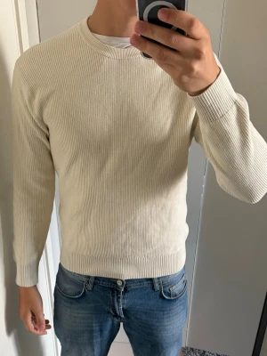 Beige ribbstickad tröja från Zara - Snygg beige ribbstickad tröja från Zara med rund halsringning och långa ärmar. Tröjan har en clean look och är tillverkad i ett mjukt material som passar perfekt till jeans eller chinos.