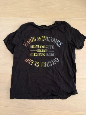 Svart Zadig & Voltaire t-shirt - Cool svart t-shirt från Zadig & Voltaire med färgglad textprint på bröstet där det står 'Art is truth' och 'Rive Droite'. T-shirten har rund hals och korta ärmar❣️