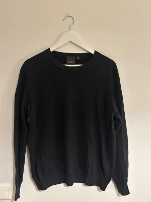 Mörkblå crewneck från Oscar Jacobson  - En stilren mörkblå tröja från Oscar Jacobson med rund halsringning och ribbade muddar vid ärmslut och nederkant. Perfekt basplagg som funkar till det mesta och har en klassisk passform. Tillverkad i mjukt material för skön känsla. Funkar otroligt bra till en skjorta under!