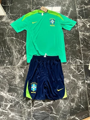 Grön Brasilien Nike träningströja - Snygg grön träningströja från Nike med Brasilien CBF-logga och gula detaljer. Tröjan har korta ärmar, rund hals och är tillverkad i ett lätt, ventilerande material som passar perfekt till fotbollsträning eller gymmet.