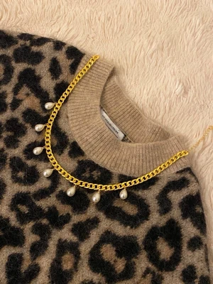 Guldhalsband med droppformade pärlor - Snyggt halsband i guldfärgad metall med sex droppformade pärlor som hänger längs kedjan. Kedjan har en chunky design och pärlorna ger en elegant touch. Perfekt accessoar för att lyfta vilken outfit som helst.